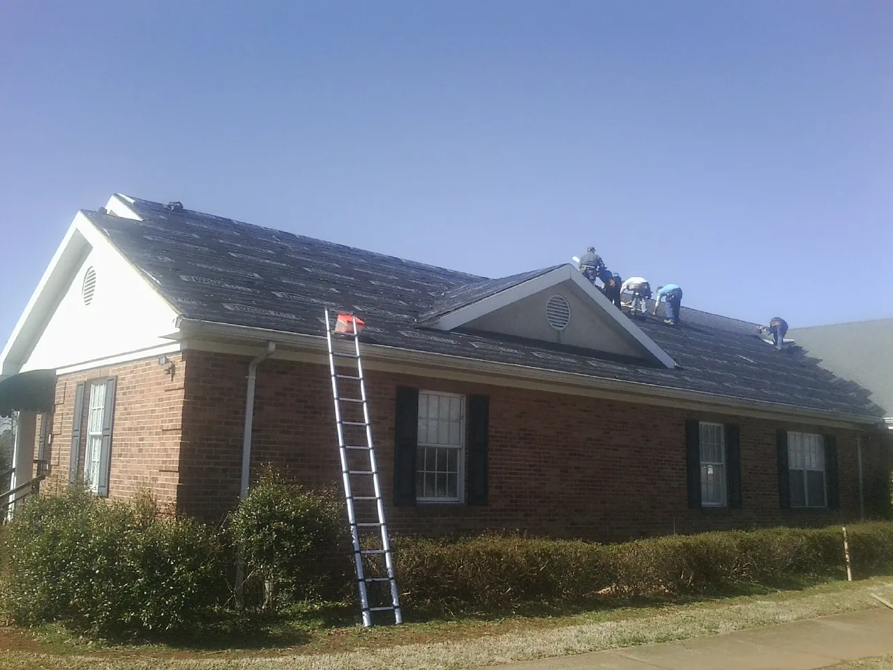 Crew tearing shingles off a brick ranch roof with a ladder set — Emergency Roof Repair work by our crew in Cornelius