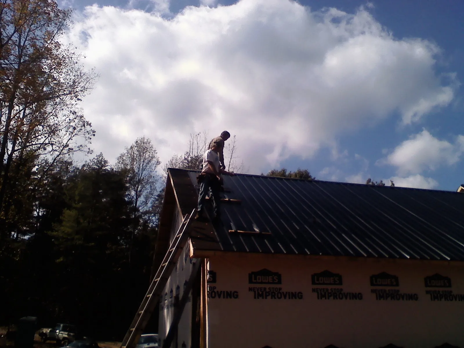 Roofer fastening dark metal panels high against a cloudy sky, from a Roof Inspection job in Cornelius