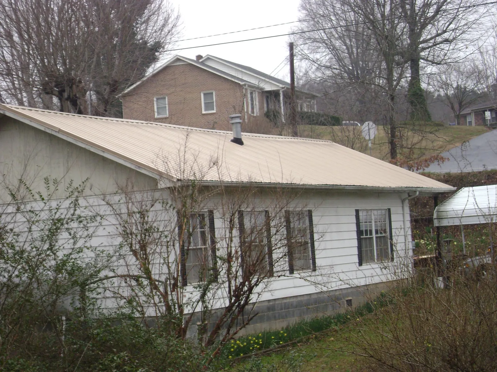 Tan metal roof on a white sided house set into a hillside — Commercial Roofing by Roofing Brothers in Cornelius